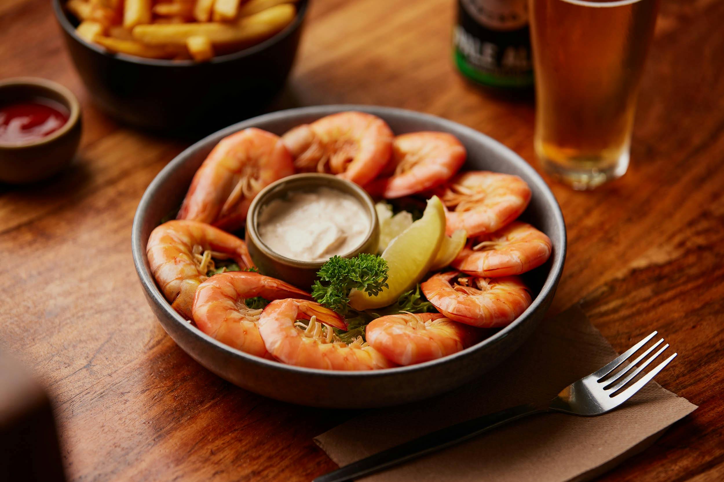 A bowl of cooked prawns and cocktail dipping sauce