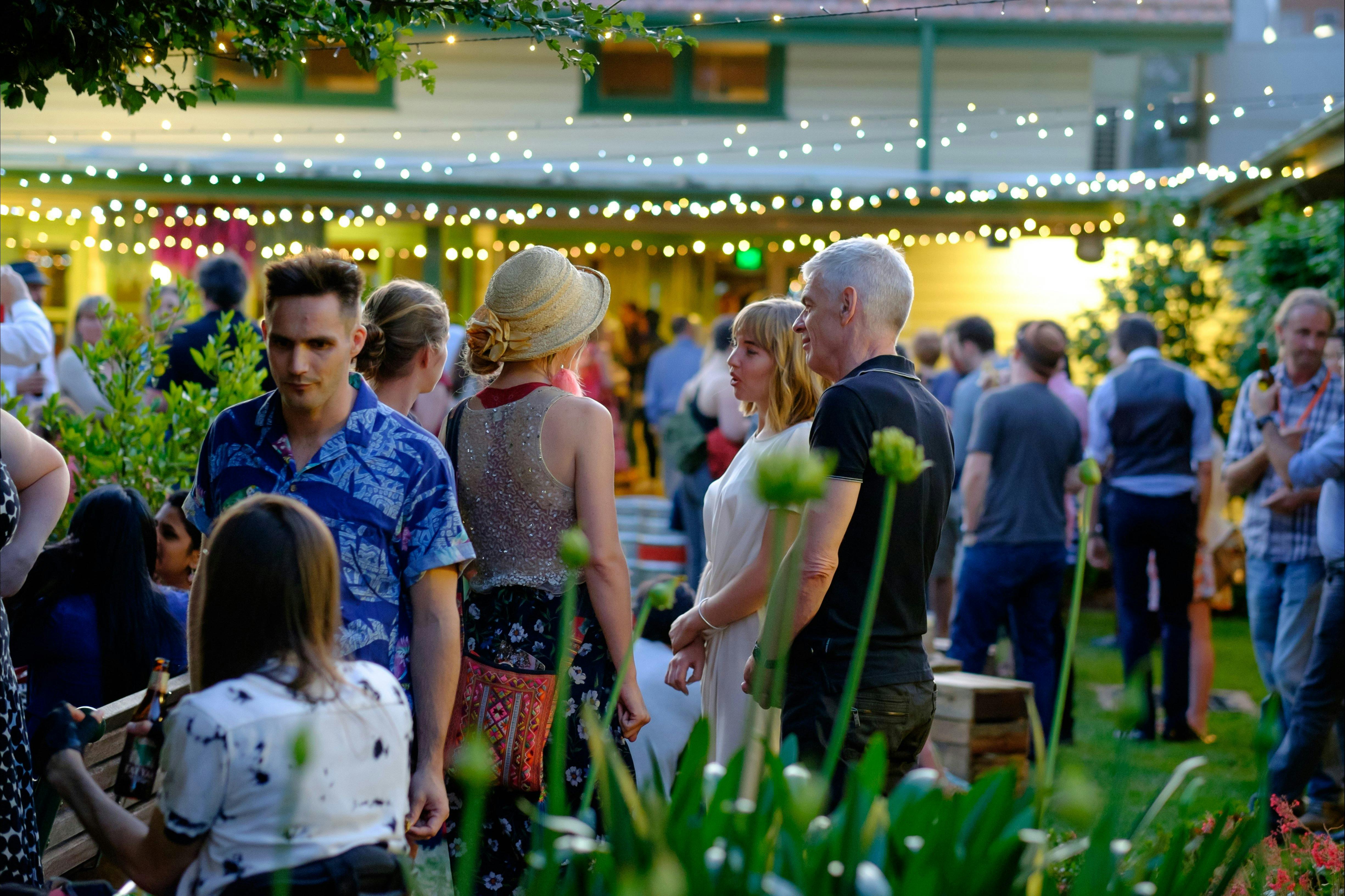 People milling in the Gorman Courtyards at twilight, surrounded by leafy foliage and fairylights