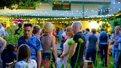 People milling in the Gorman Courtyards at twilight, surrounded by leafy foliage and fairylights