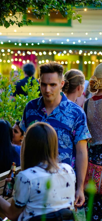 People milling in the Gorman Courtyards at twilight, surrounded by leafy foliage and fairylights