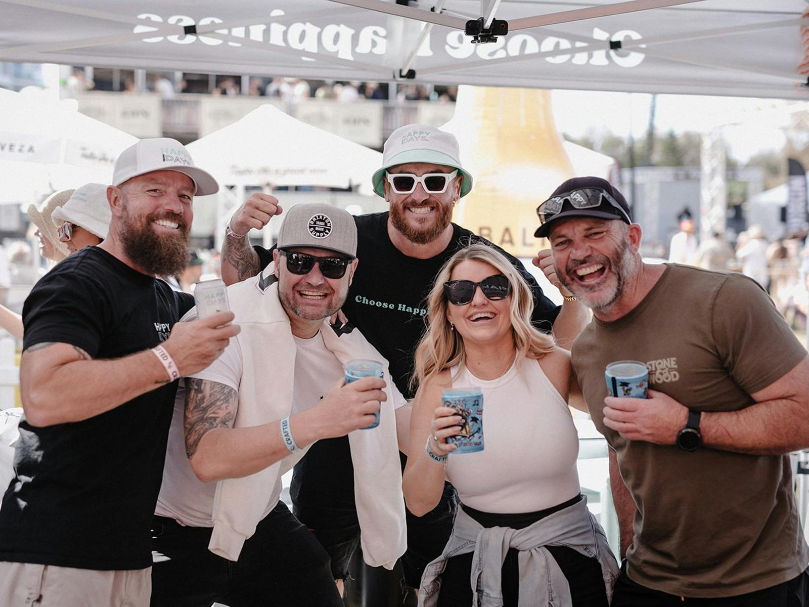 A group of 5 people standing near each other holding beers