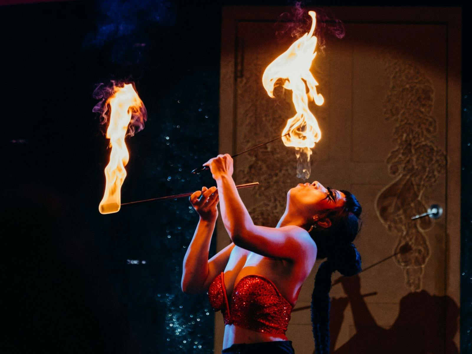A fire performer eating fire from one wand while holding a second flaming wand aloft