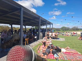 Families and friends relaxing on picnic rugs and enjoying live music under festoon lights outside th