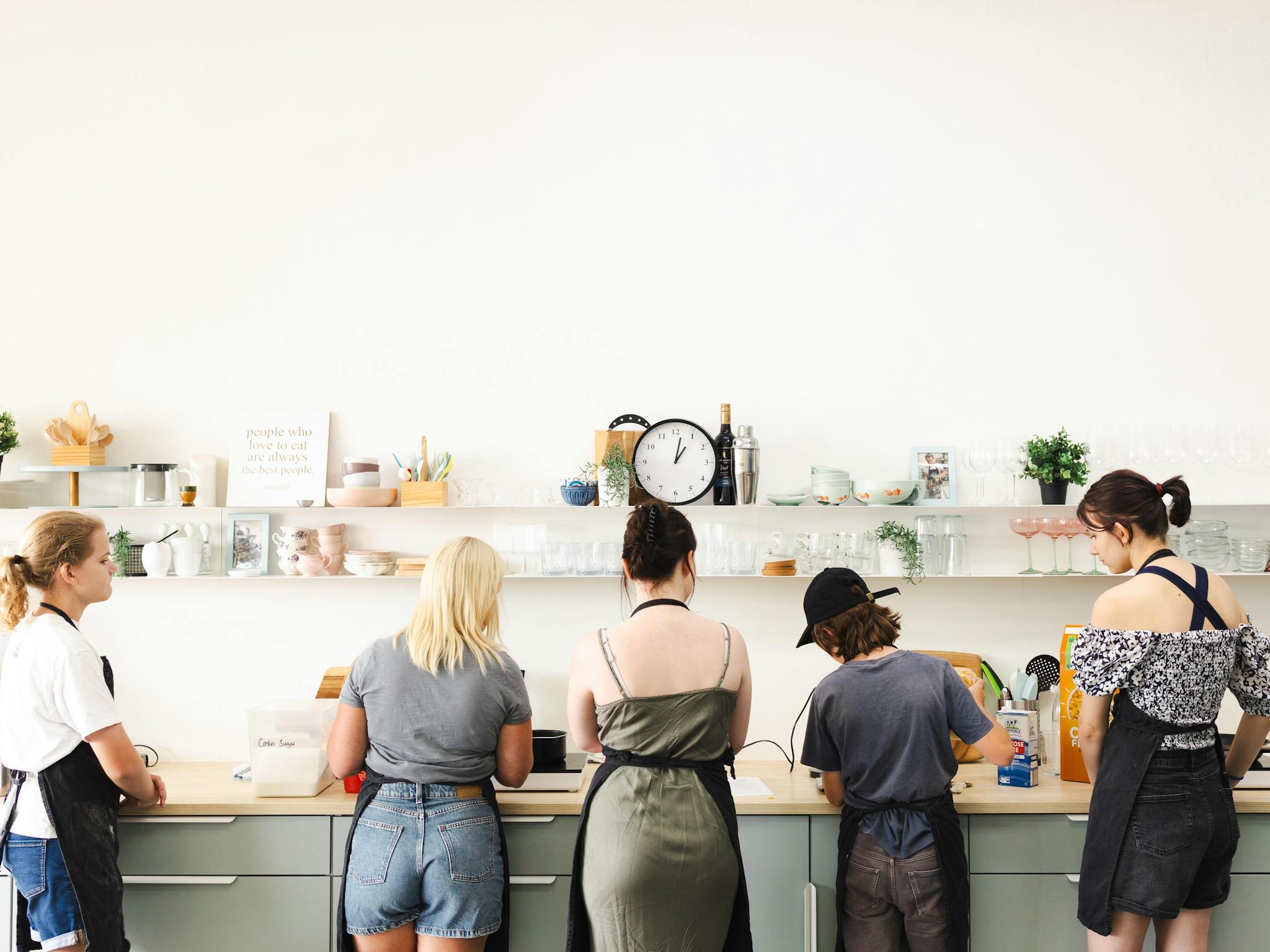 five people standing at a kitchen bench, cooking. five people standing at a kitchen bench, cooking.