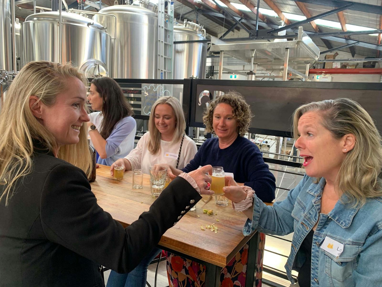 Two women raising their beer glasses and smiling at each other