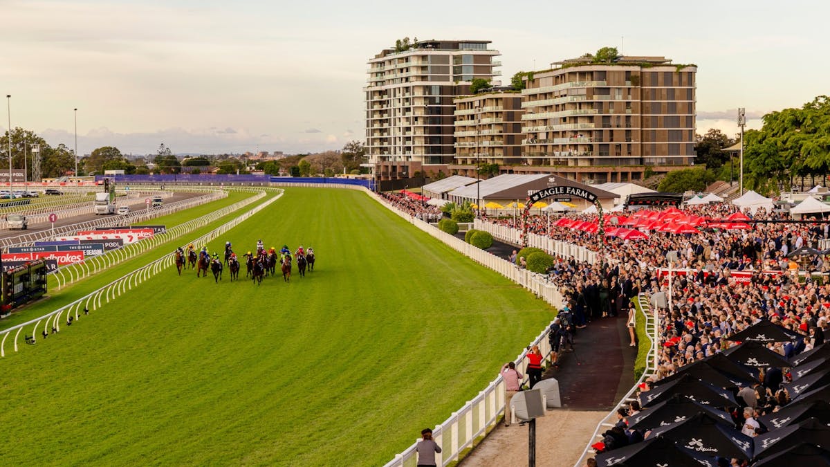 A wide shot of horses running on a track with a large crowd watching