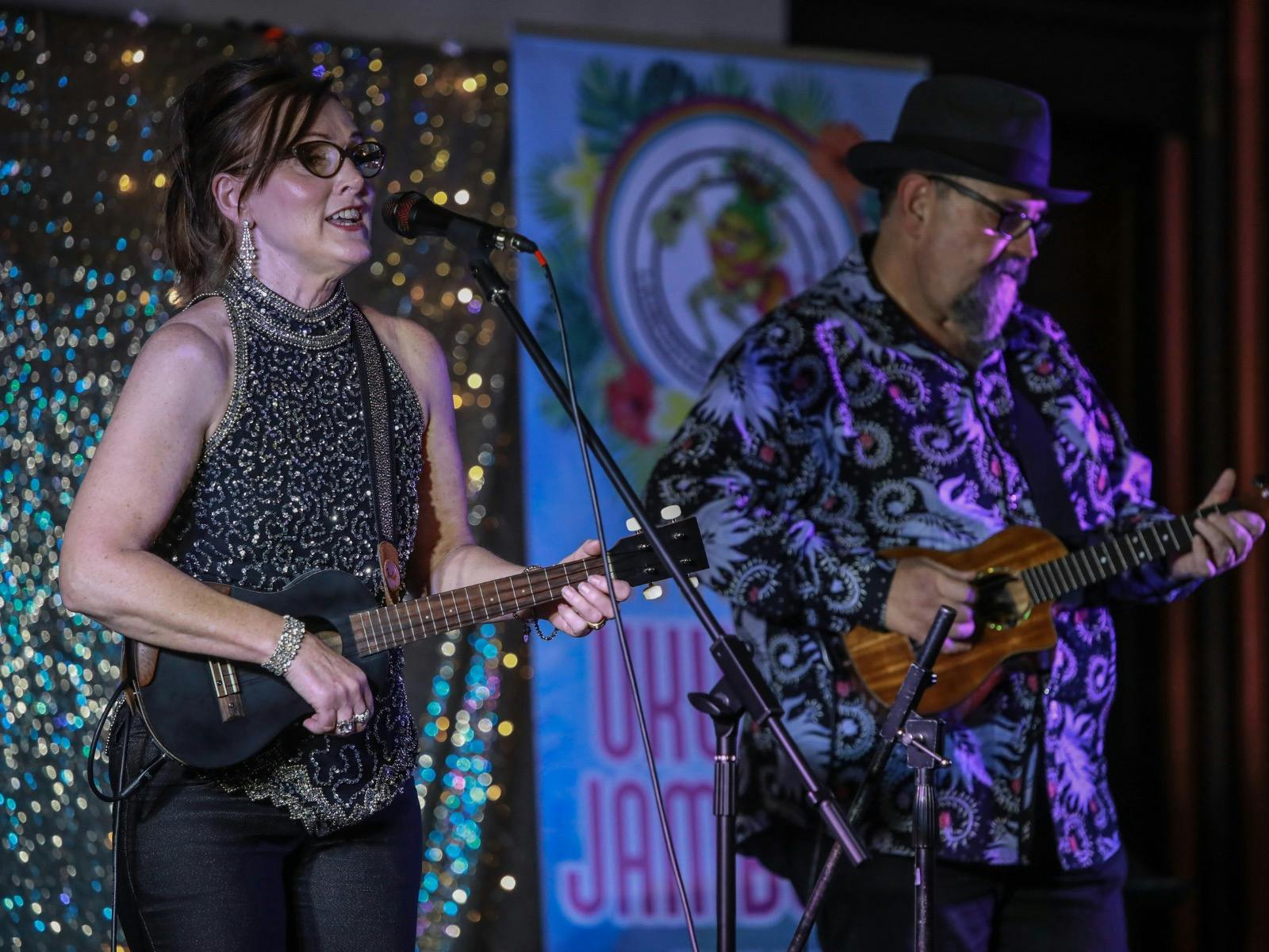 Ukulele duo in sparkly clothing against a glitter backdrop performing at evening concert.