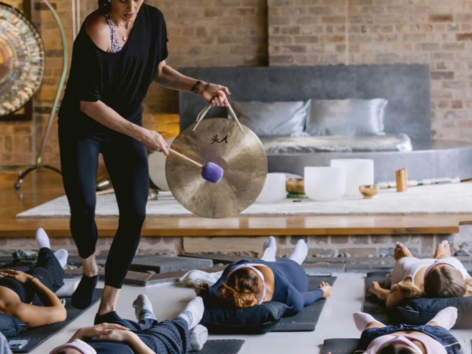 Photo of Natalie Grace playing a gong over sound bath guests.