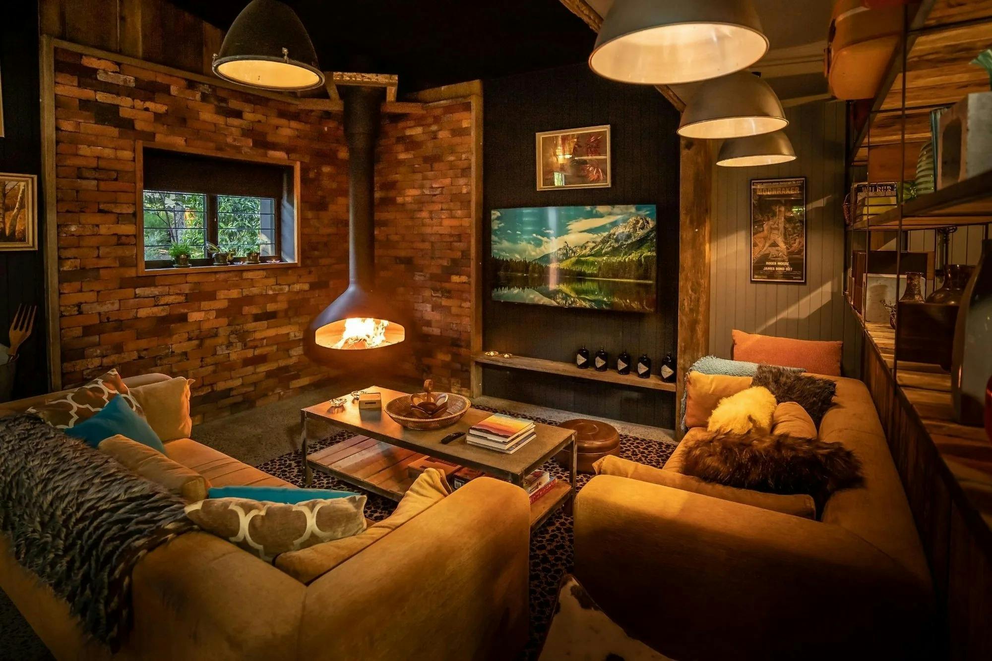 Lounge with leather sofas, a lit suspended fireplace and brick and timber walls