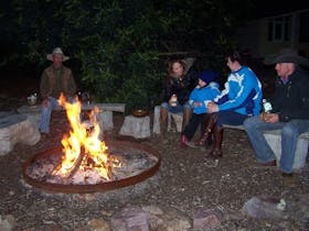adults & children sitting on log seats around large campfire