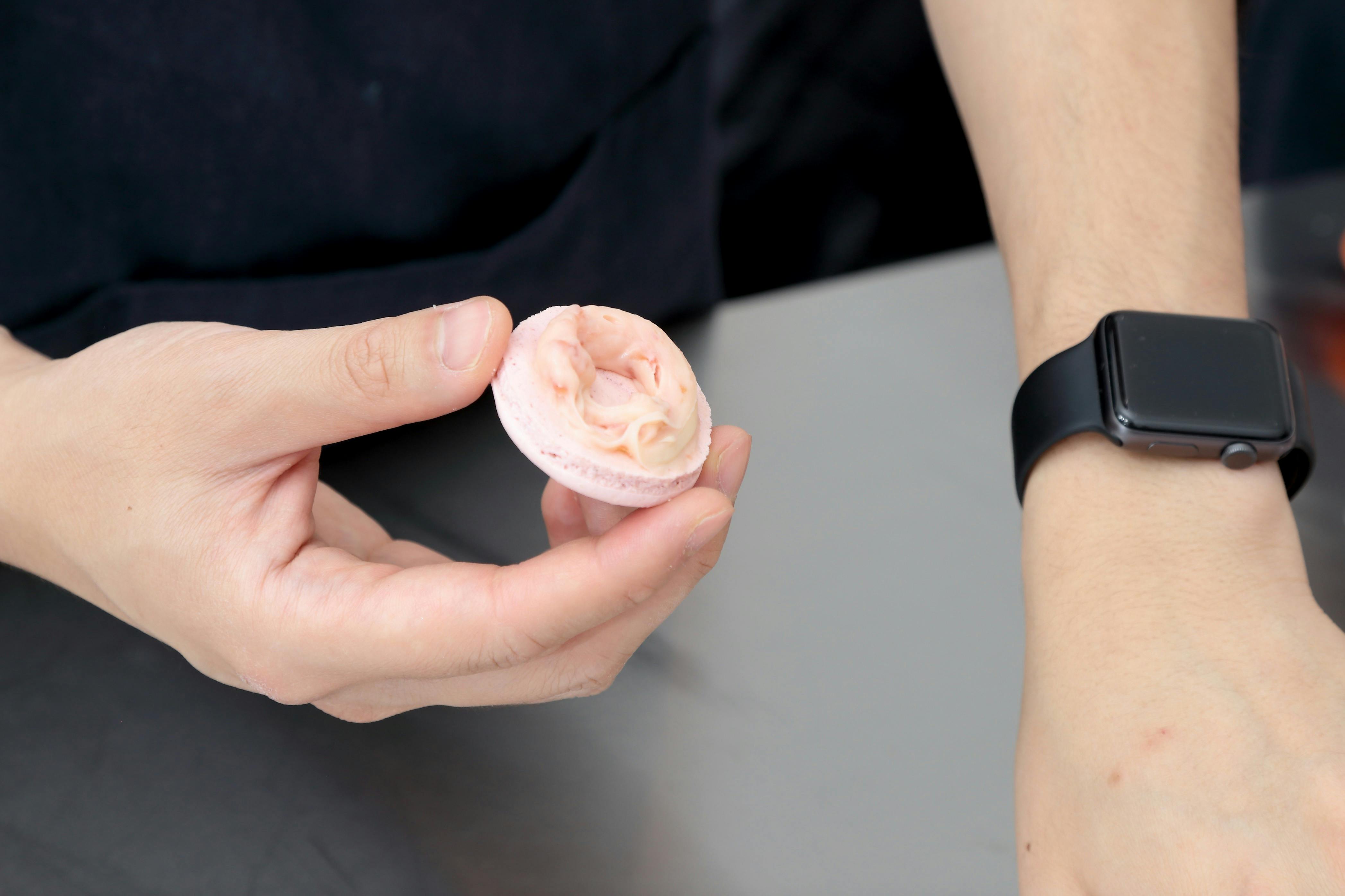 a hand holding a pink macaron shell