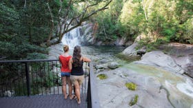 Two people standing on deck overlooking falls and pool.