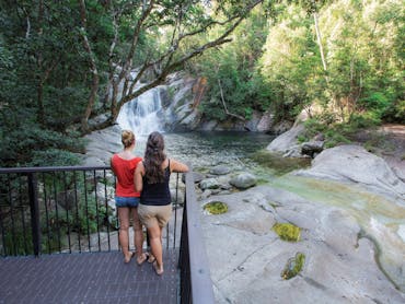 Two people standing on deck overlooking falls and pool.