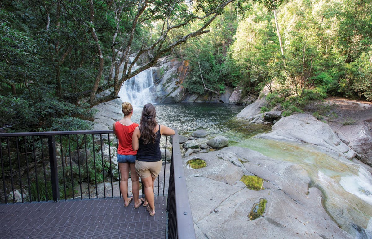 Two people standing on deck overlooking falls and pool.