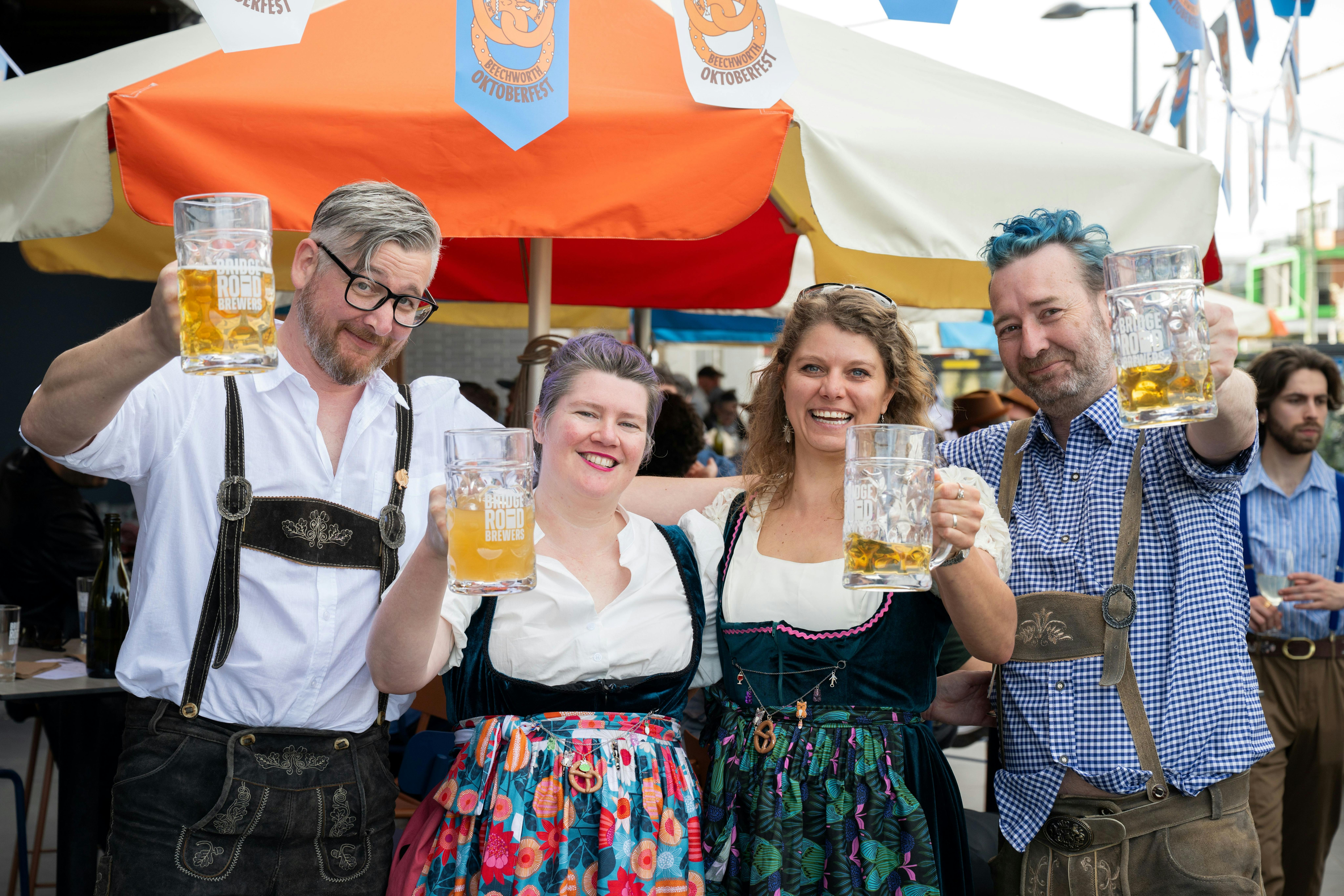 Group of men and women in traditional Oktoberfest outfits cheering and raising glasses