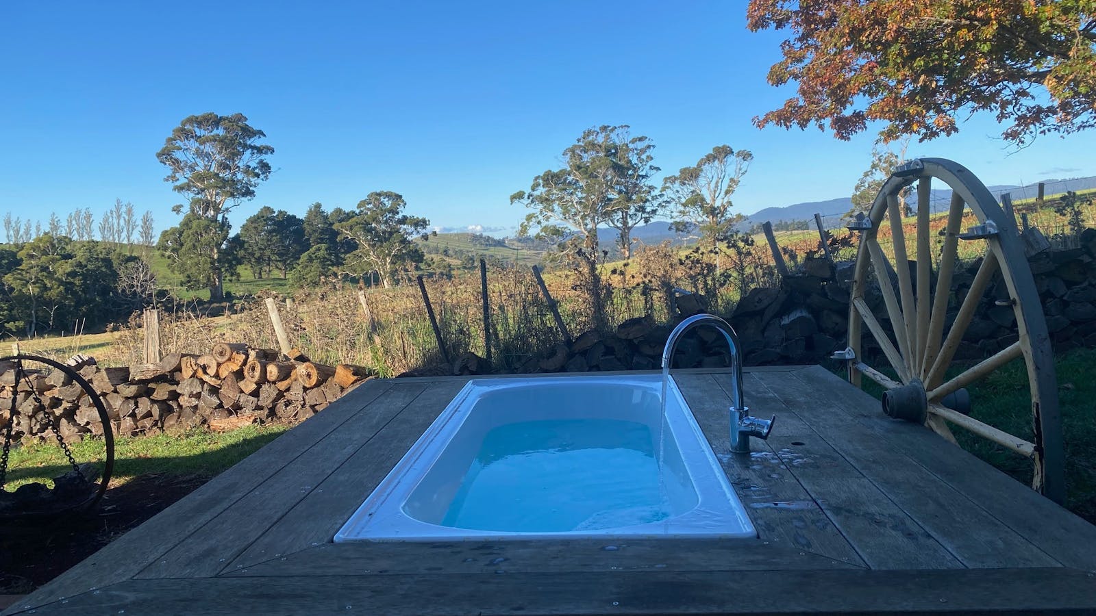 A sunken outdoor bath nestled into a private timber deck, overlooking rolling farmland and open coun