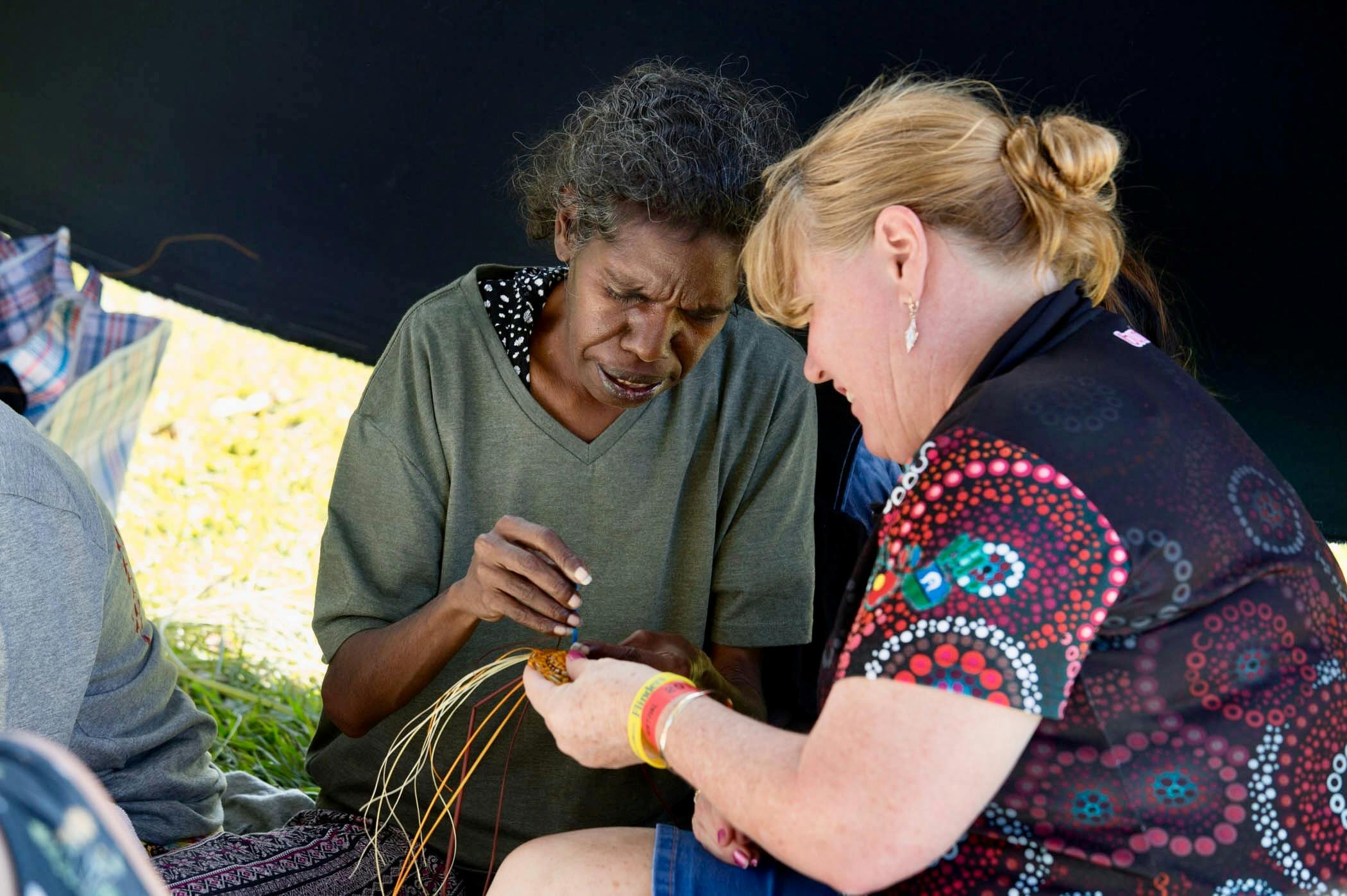 A woman teaching another women how to weave with pandanus