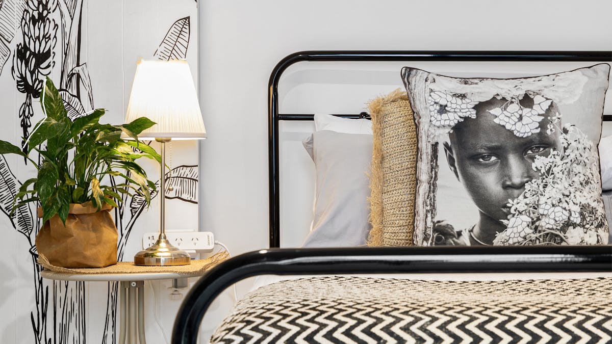 close up of queen bed, art of a banana tree by the owner, cushions and pillows
