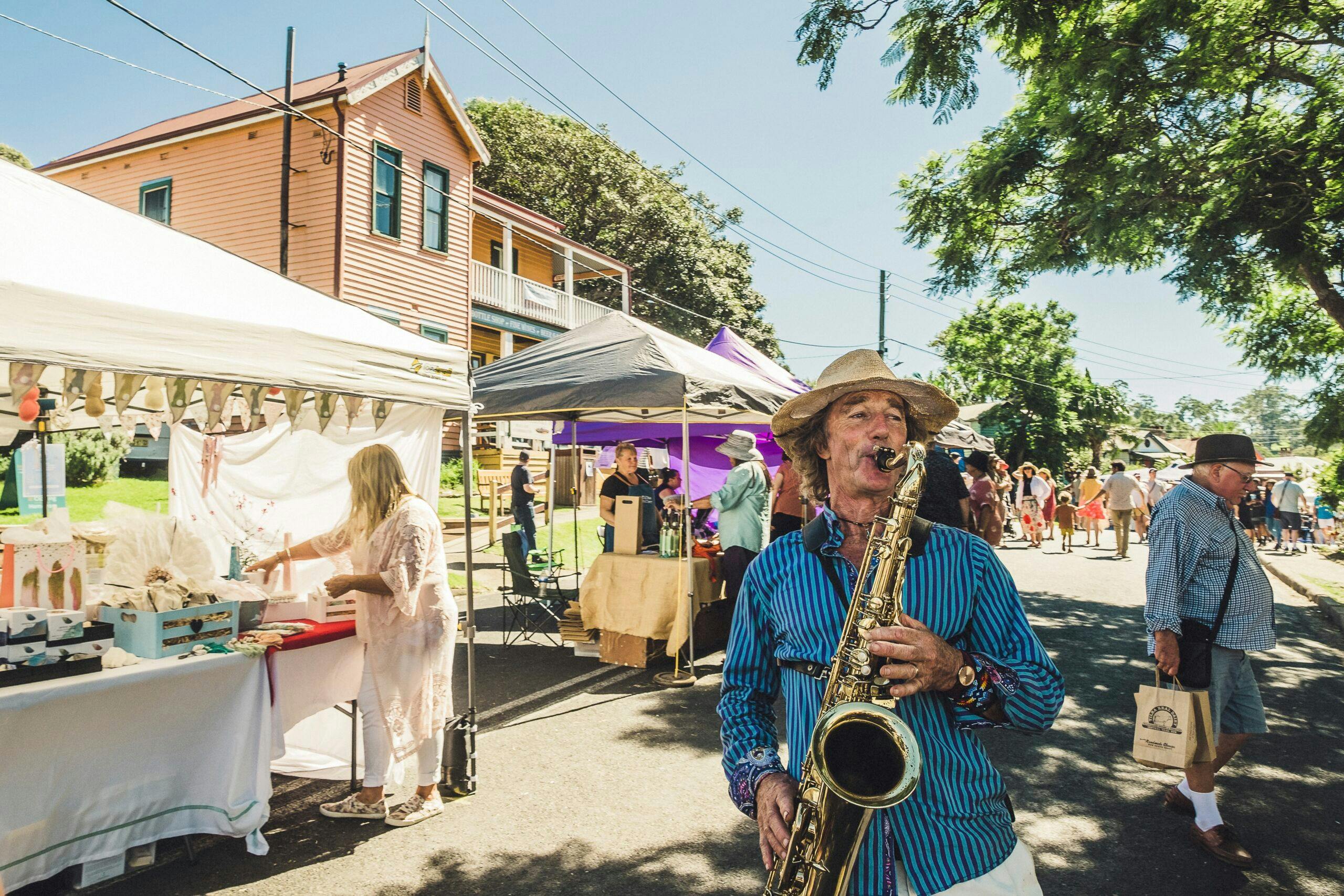 Saxophone player performs on the street with market stalls in background