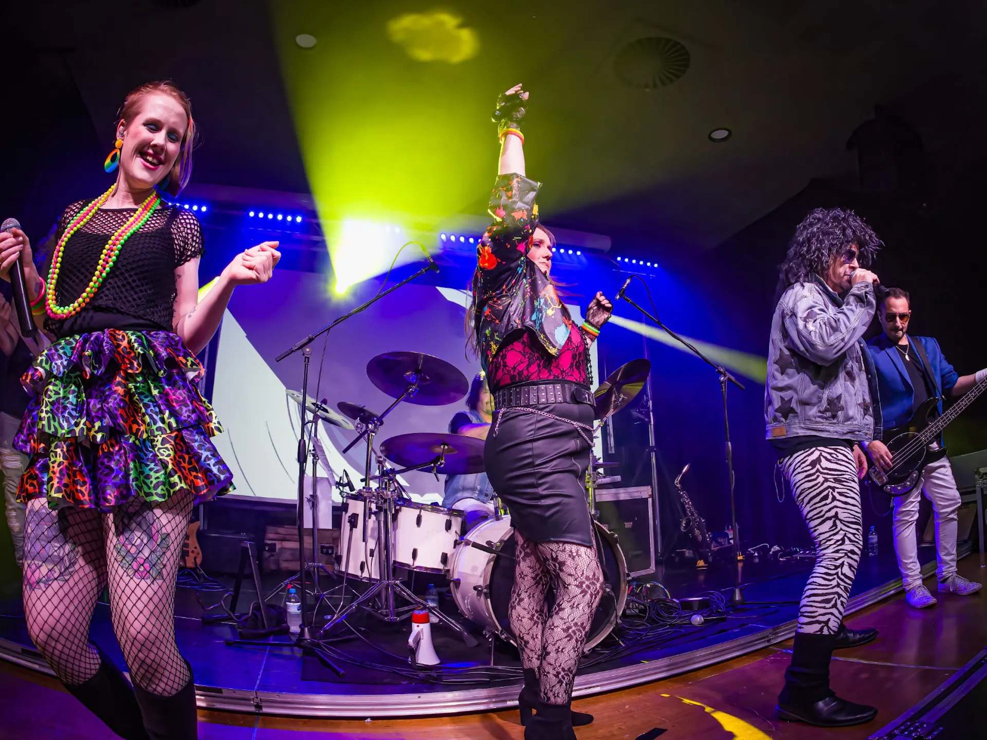 Musicians on stage during a performance. In 80s style clothing