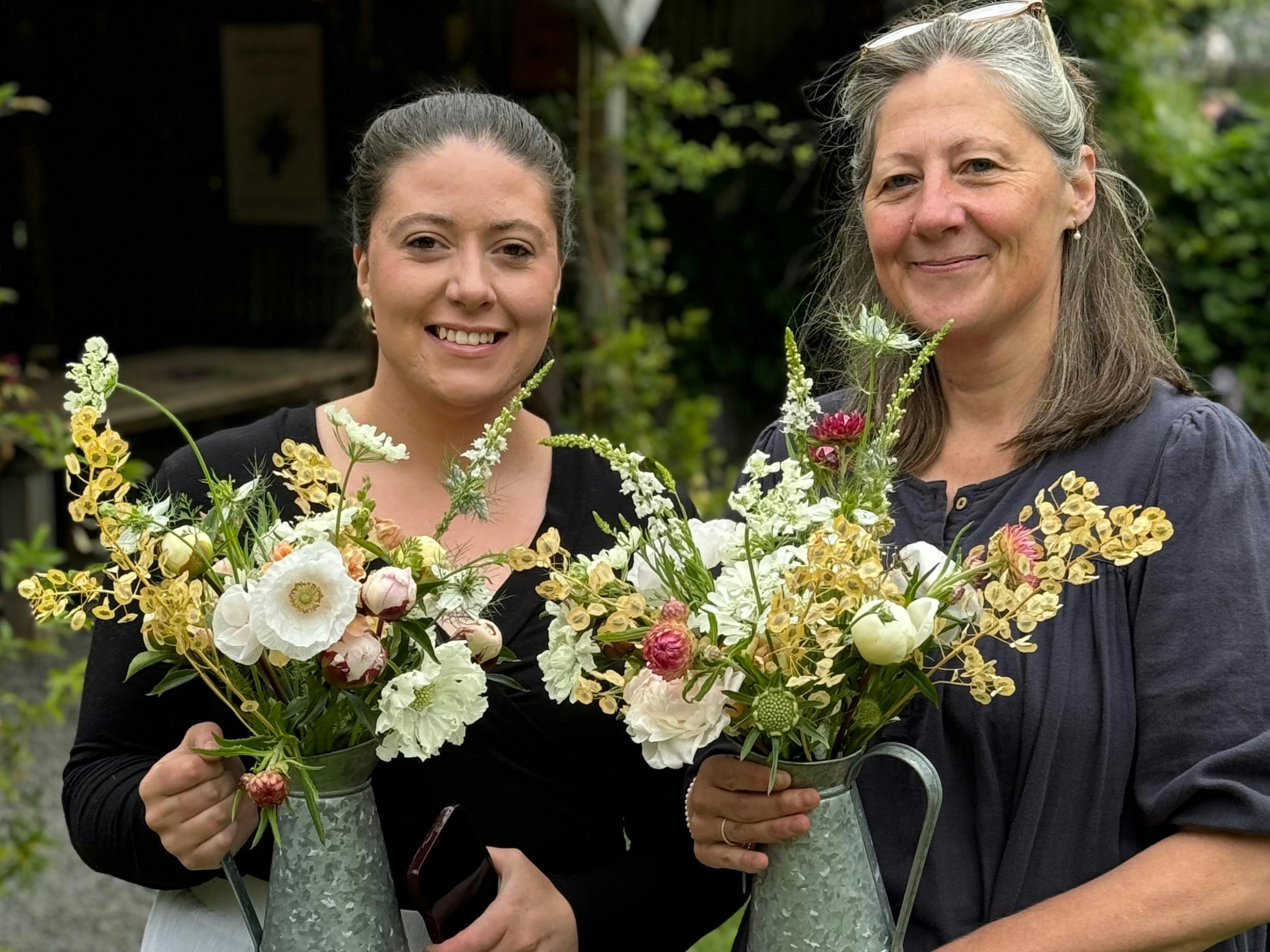 Two people smiling holding large bouquets of colourful flowers.