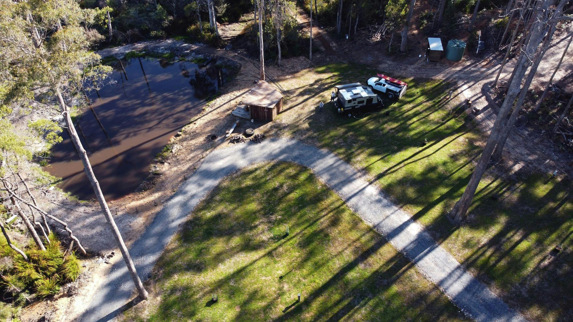 Camp sites from overhead shot by a drone, with shadows of Tasmanian bush over lush green camp sites
