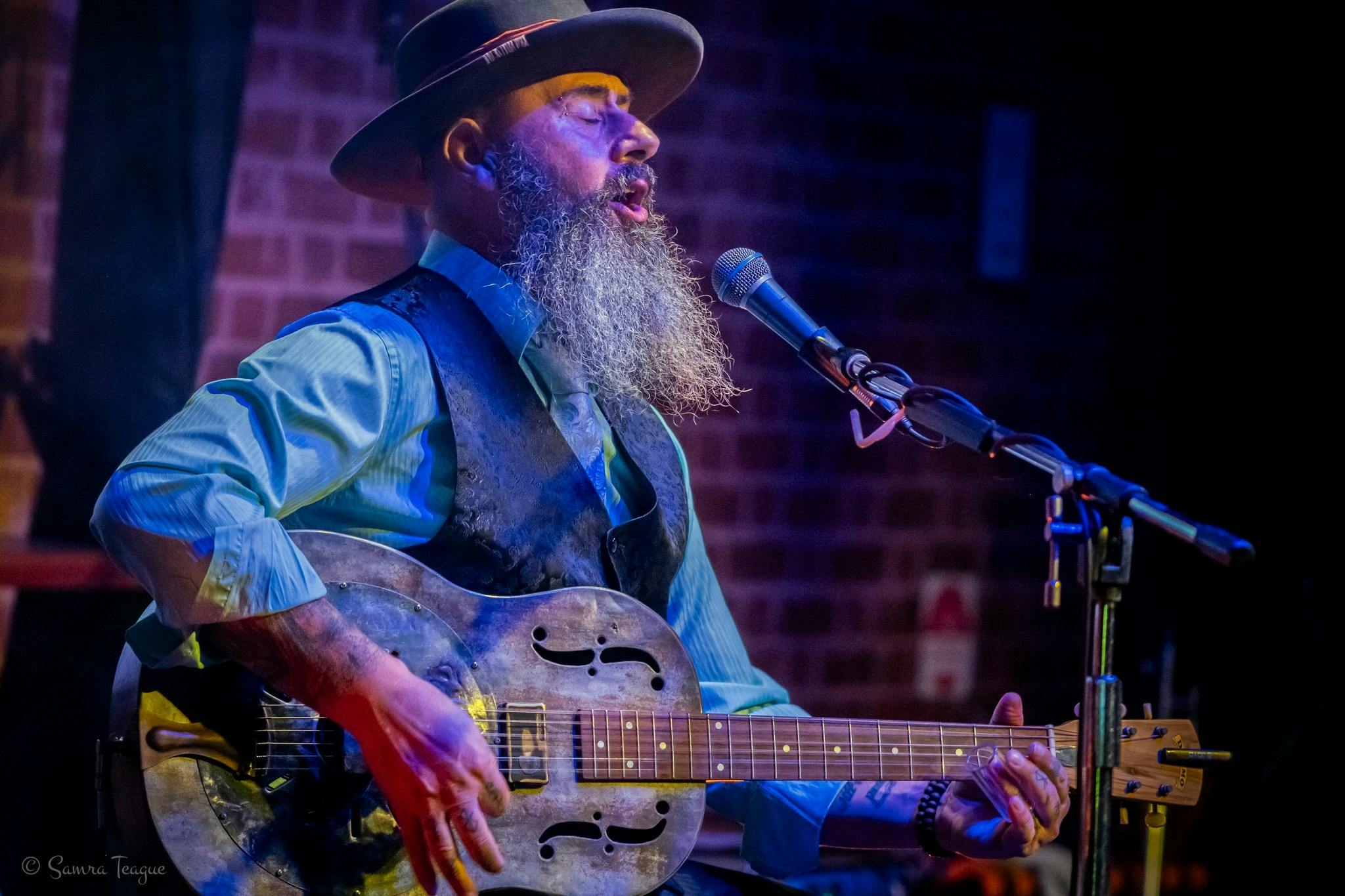 A man singing with a guitar and a hat
