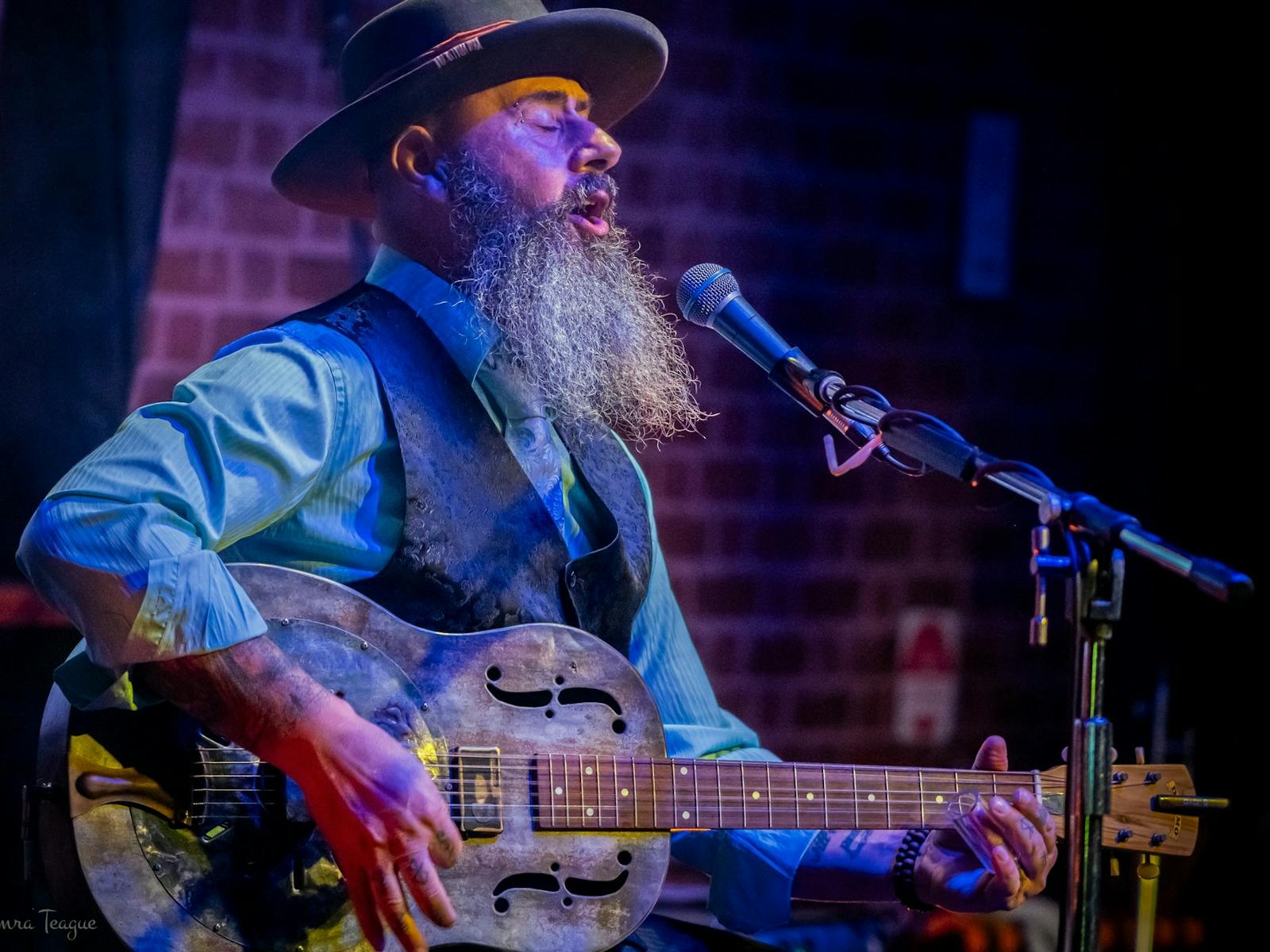 A man singing with a guitar and a hat