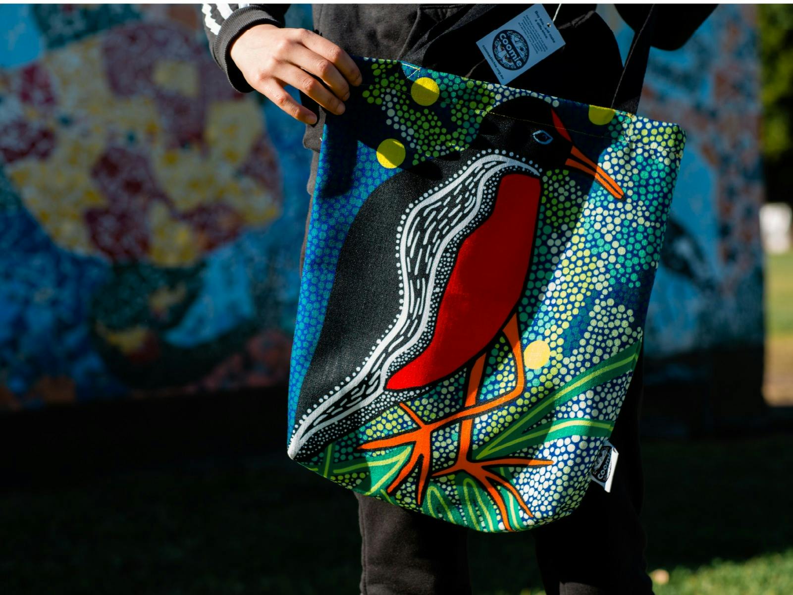 Girl holding up a colourful tote bag featuring an artwork of a water hen