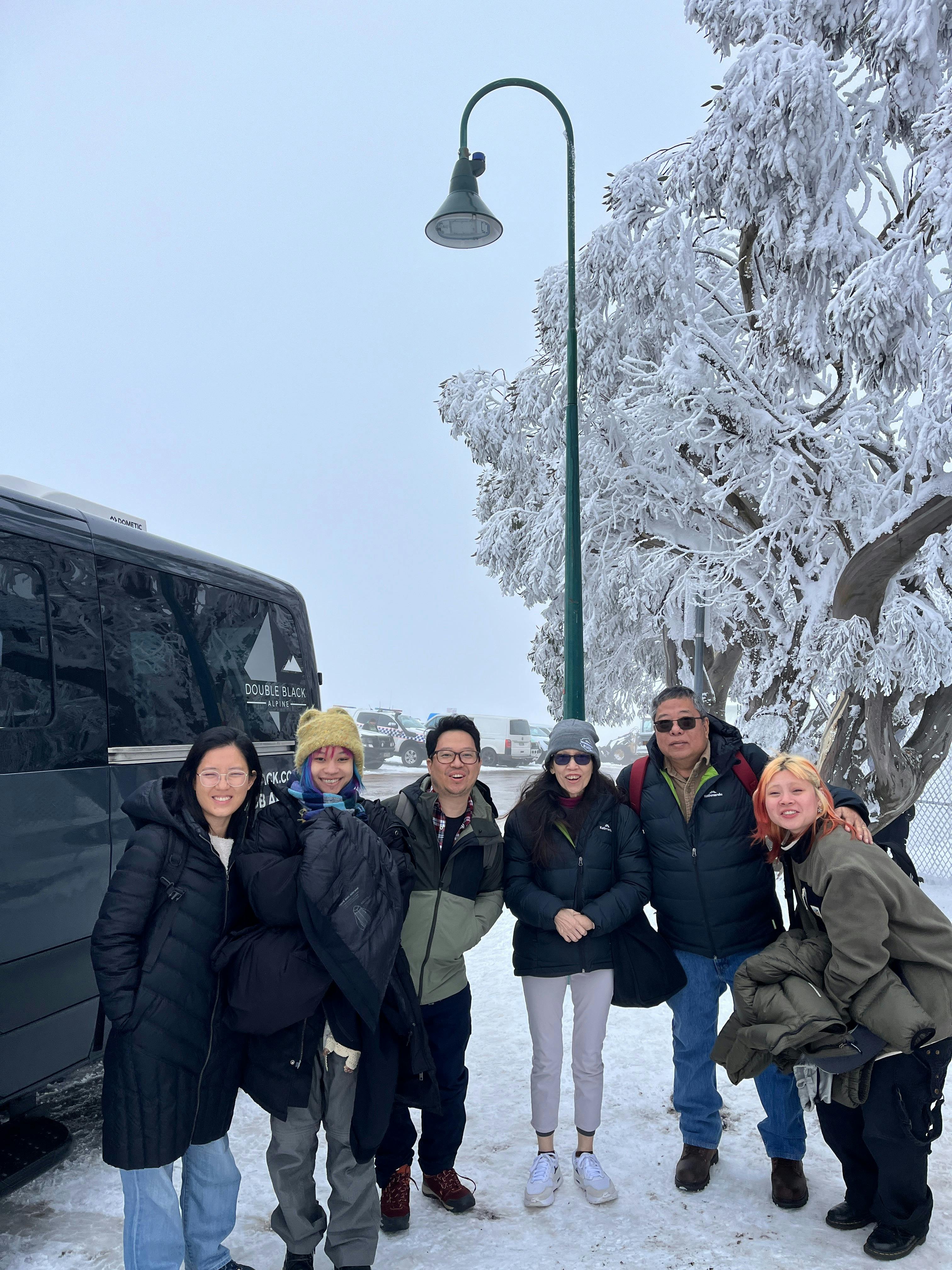 Guests standing in the snow on Mount Buller next to Double Black Alpine passenger van