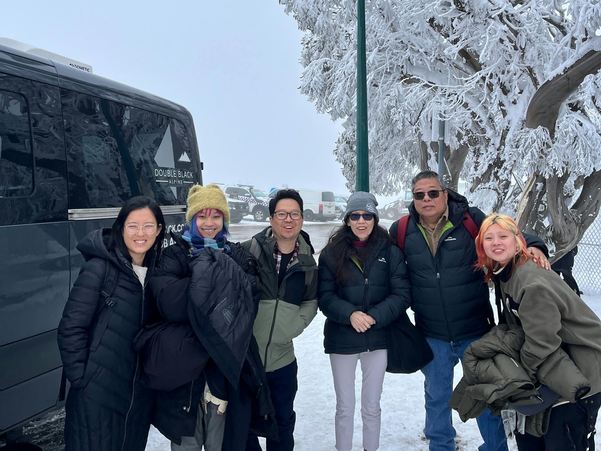 Guests standing in the snow on Mount Buller next to Double Black Alpine passenger van