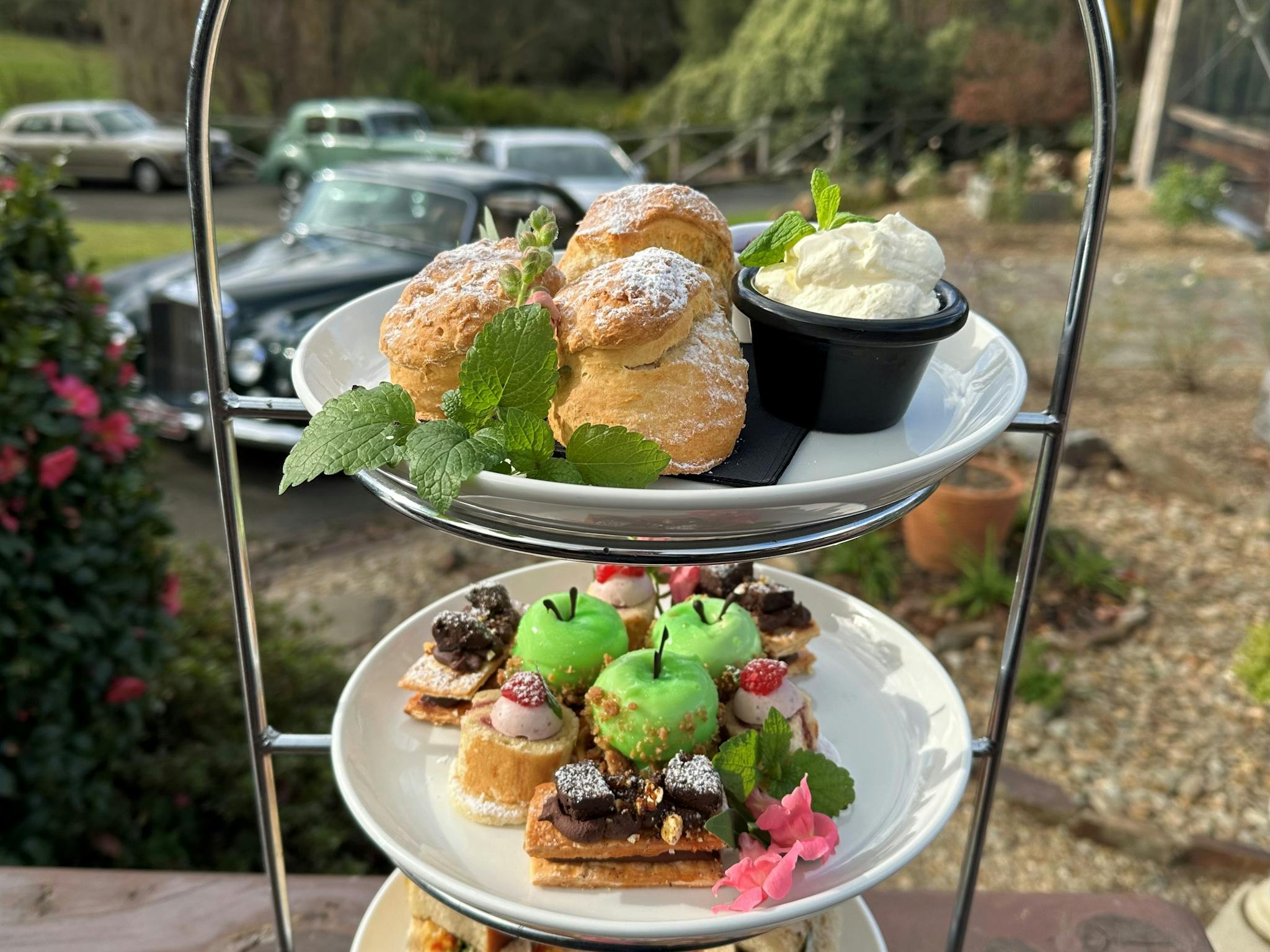 A three tiered stand of high tea sweet and savoury pastries, scones jam and cream.