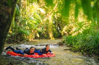 2 people laying on red river sleds, floating through the river