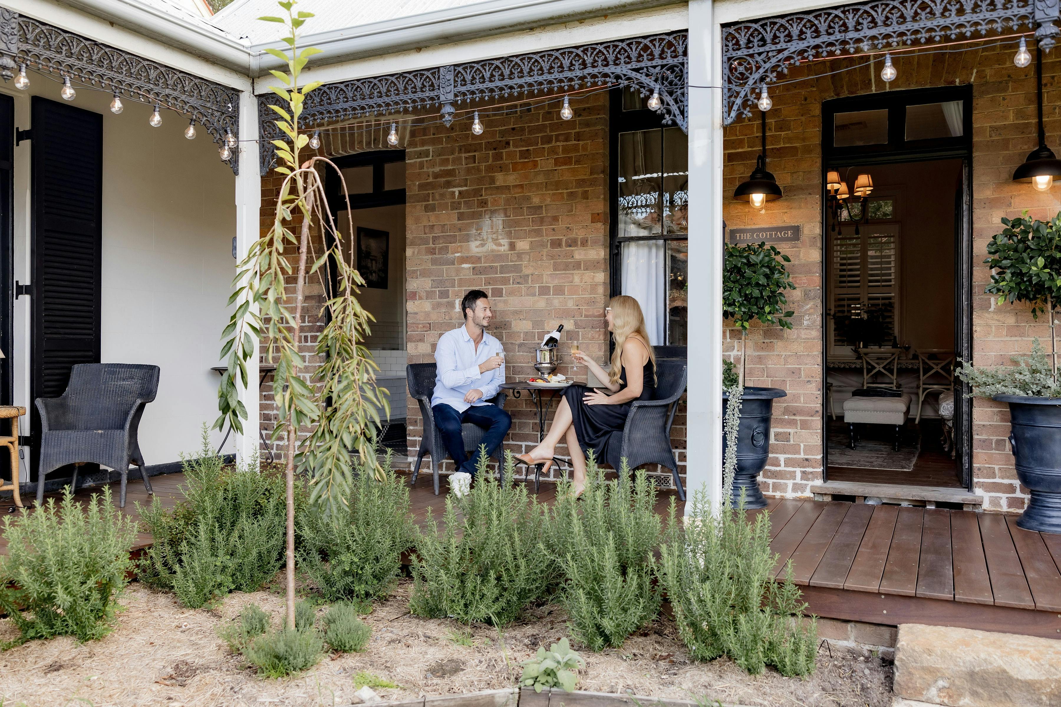 Two people enjoying a drink on a porch in front of a garden