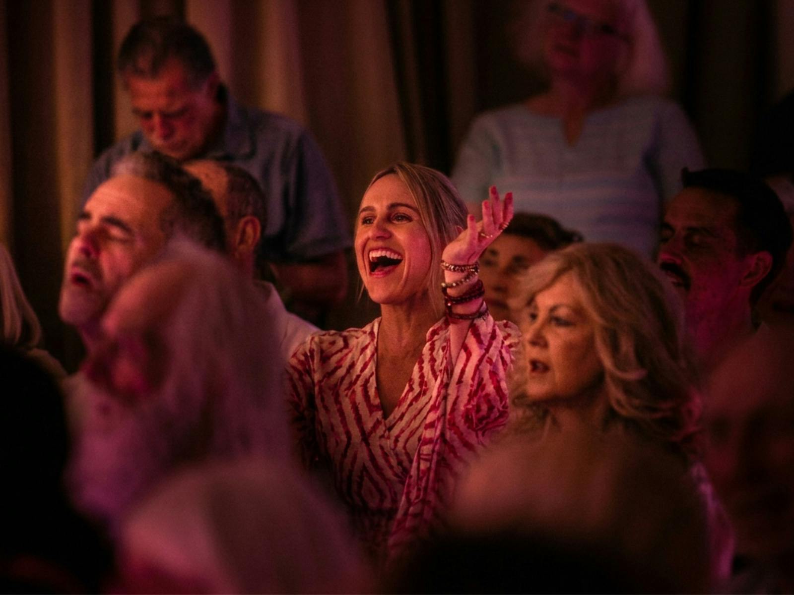 A woman with arms up, singing, smiling