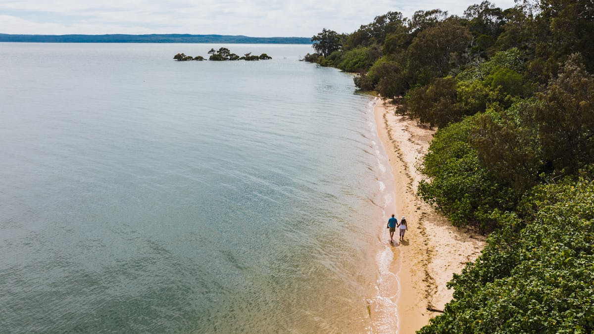 Aerial view of couple walking hand in hand on a sunny secluded Coochiemudlo Island beach