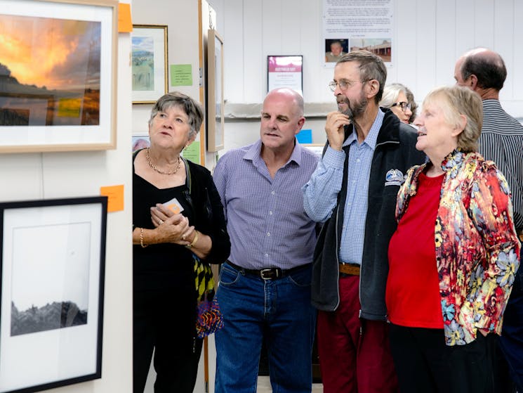 four people viewing photographs hanging on art show boards