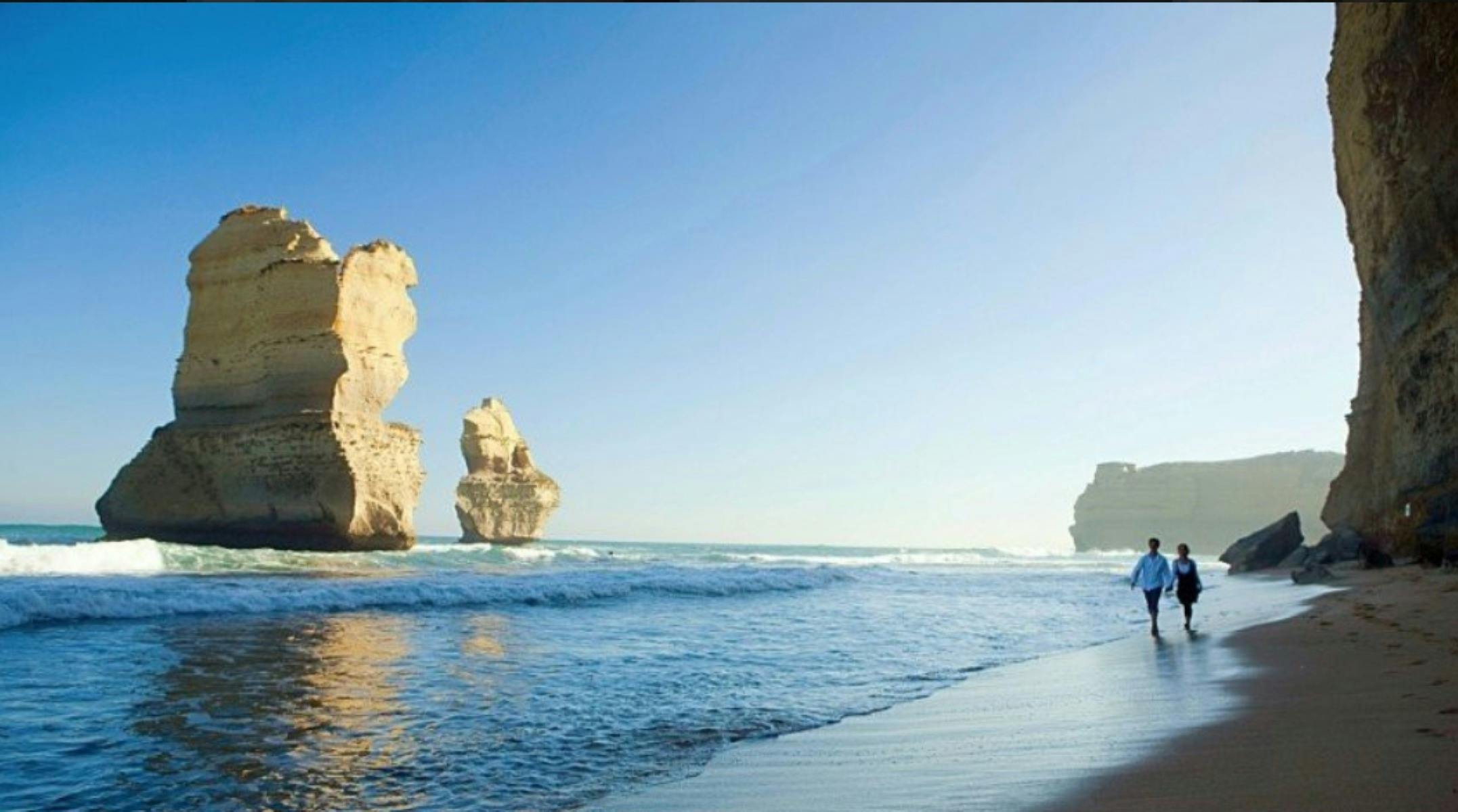 Blue sky, couple walking along beach near 12 some of the 12 apostles