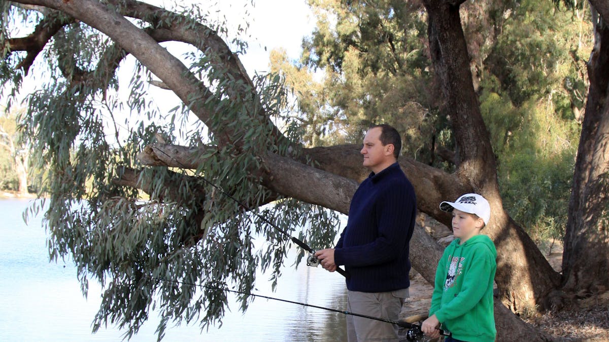 A man and a boy are standing on the bank of the Goondiwindi Water Park, fishing in the water