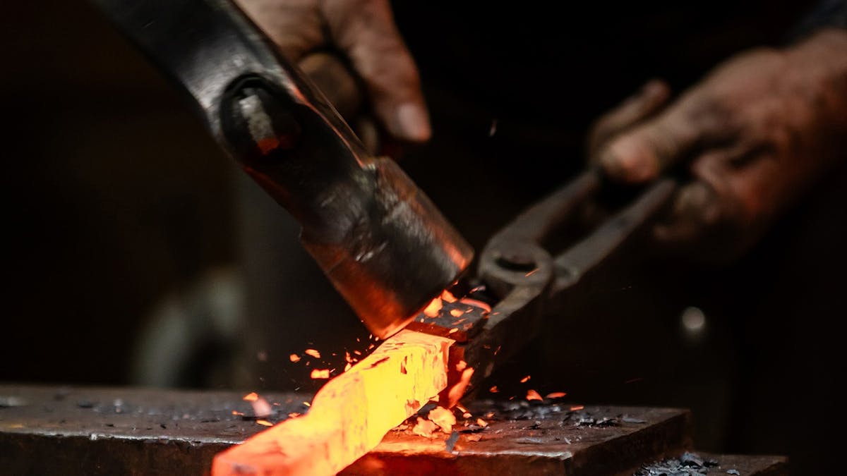 Hammer striking heated metal on anvil. Hammer striking heated metal on anvil.