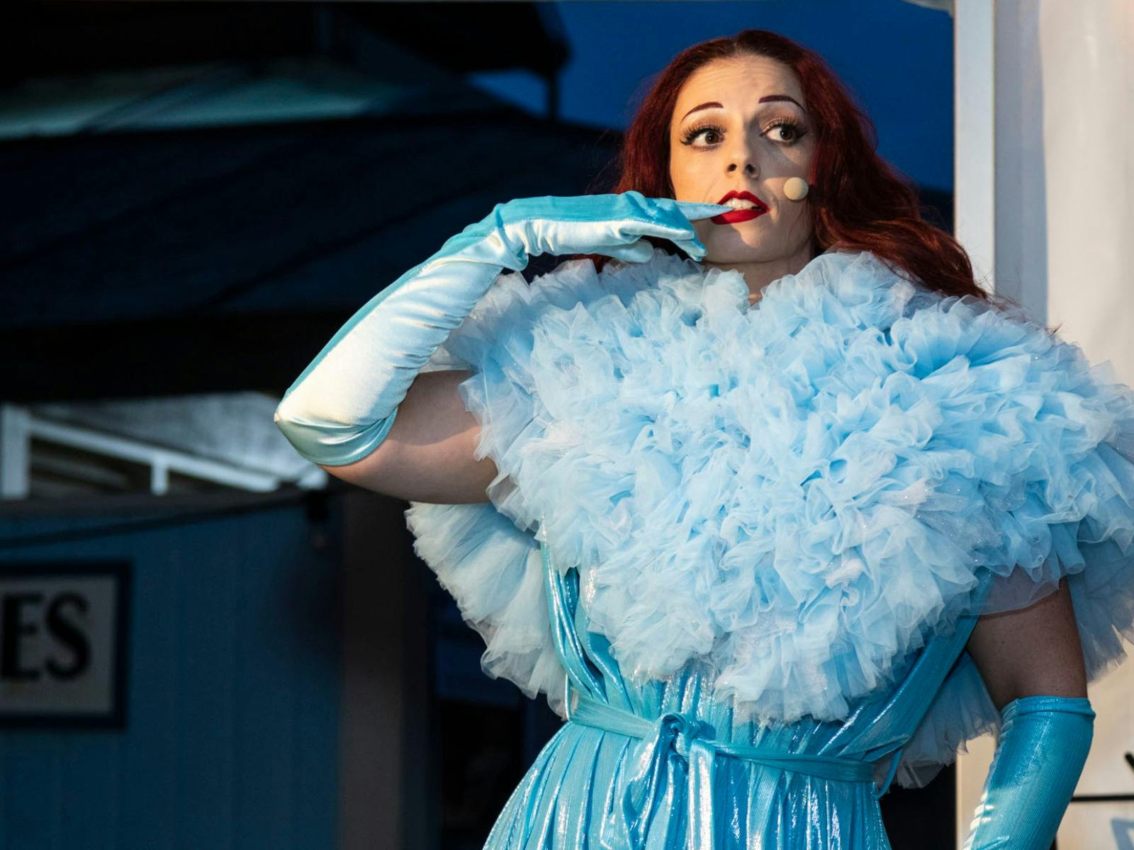 Woman in powder blue fluffy dress removes her own glove with her teeth