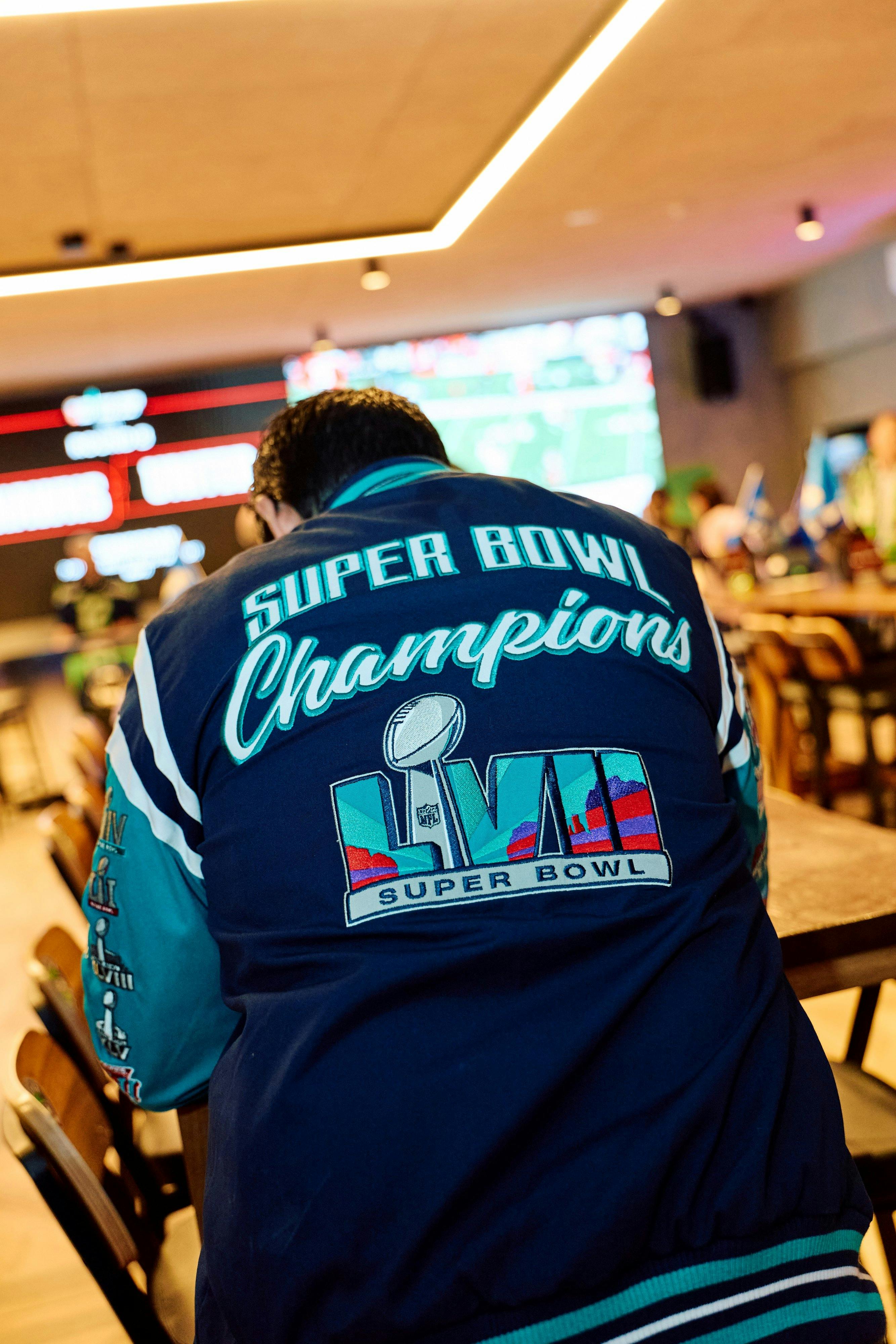 a person wearing a letterman jacket with text displaying super bowl champions