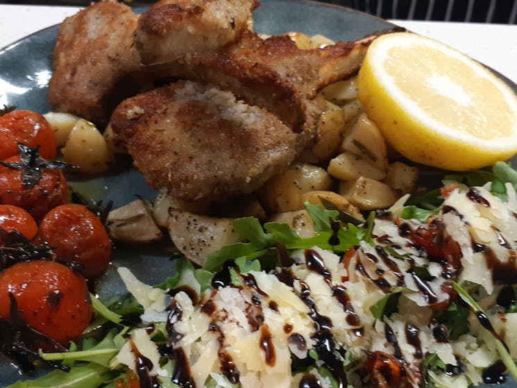 Lamb Cutlets Confit tomatoes, roast potatoes and salad on blue plateoes