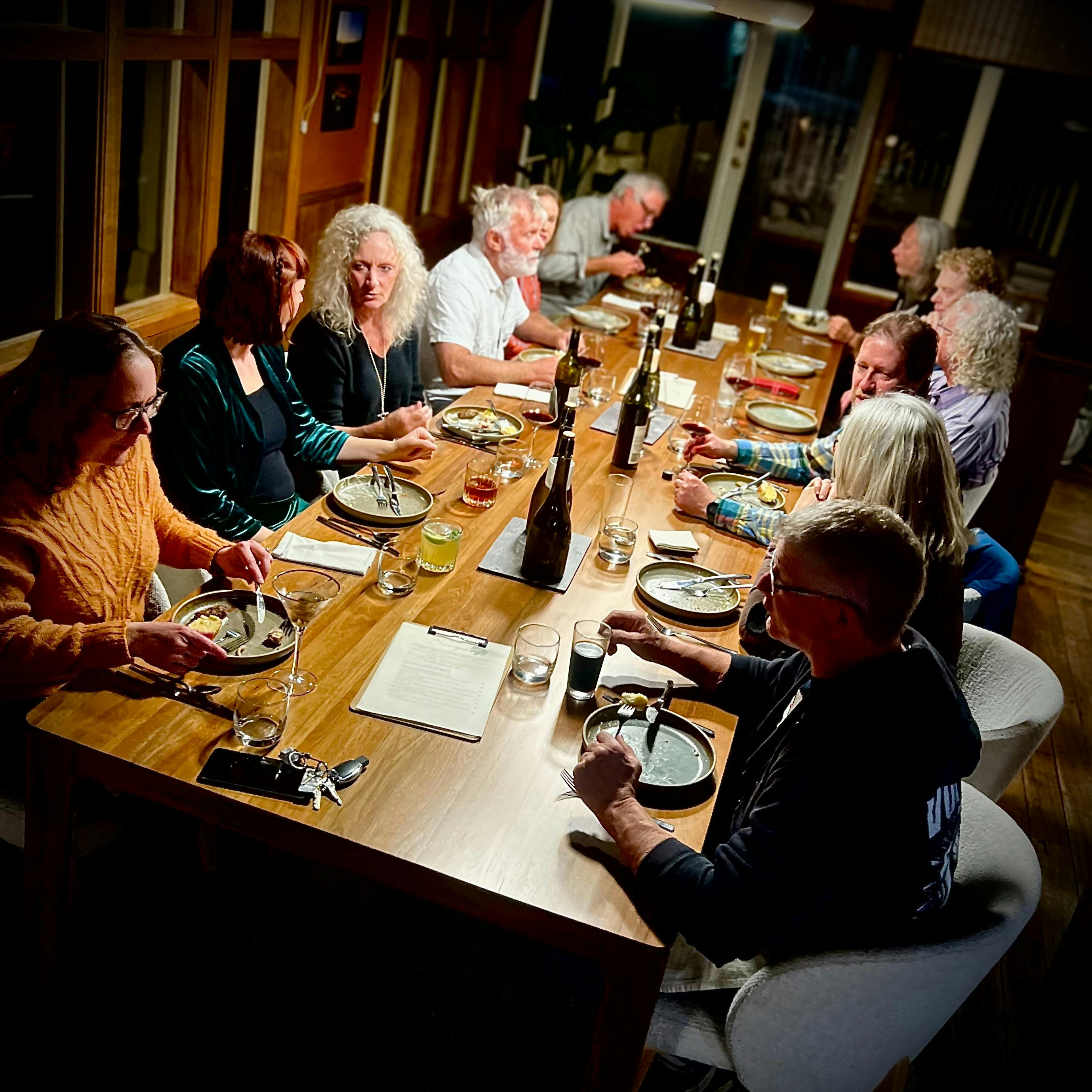 a social gathering around the Host's Table with people enjoying food, wine & conversation.