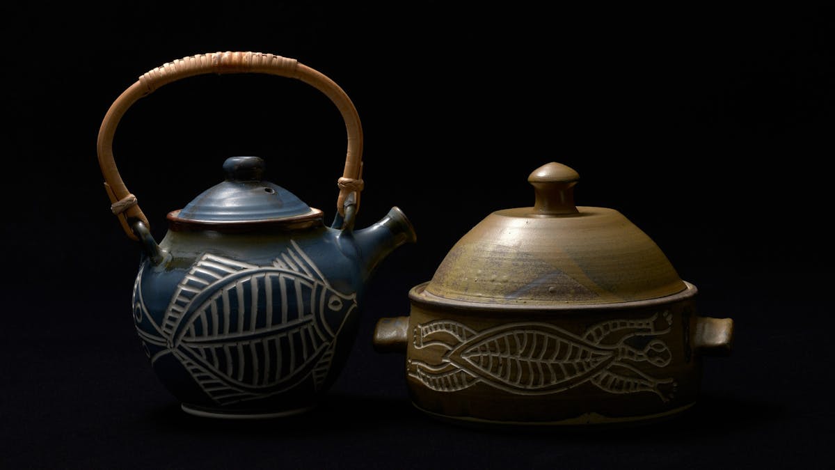Dramatically lit portrait of a glazed stoneware casserole and teapot