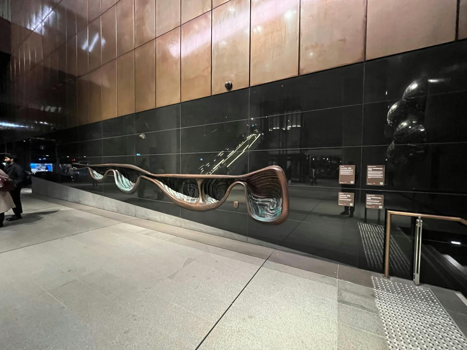 Sculptural artwork along a dark tiled wall inside a Sydney Metro station.
