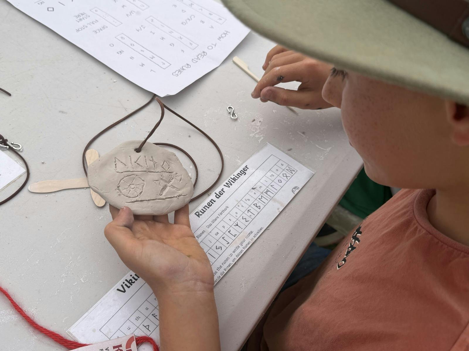 A boy studies his hand-made clay amulet, inscribed with Viking runes.