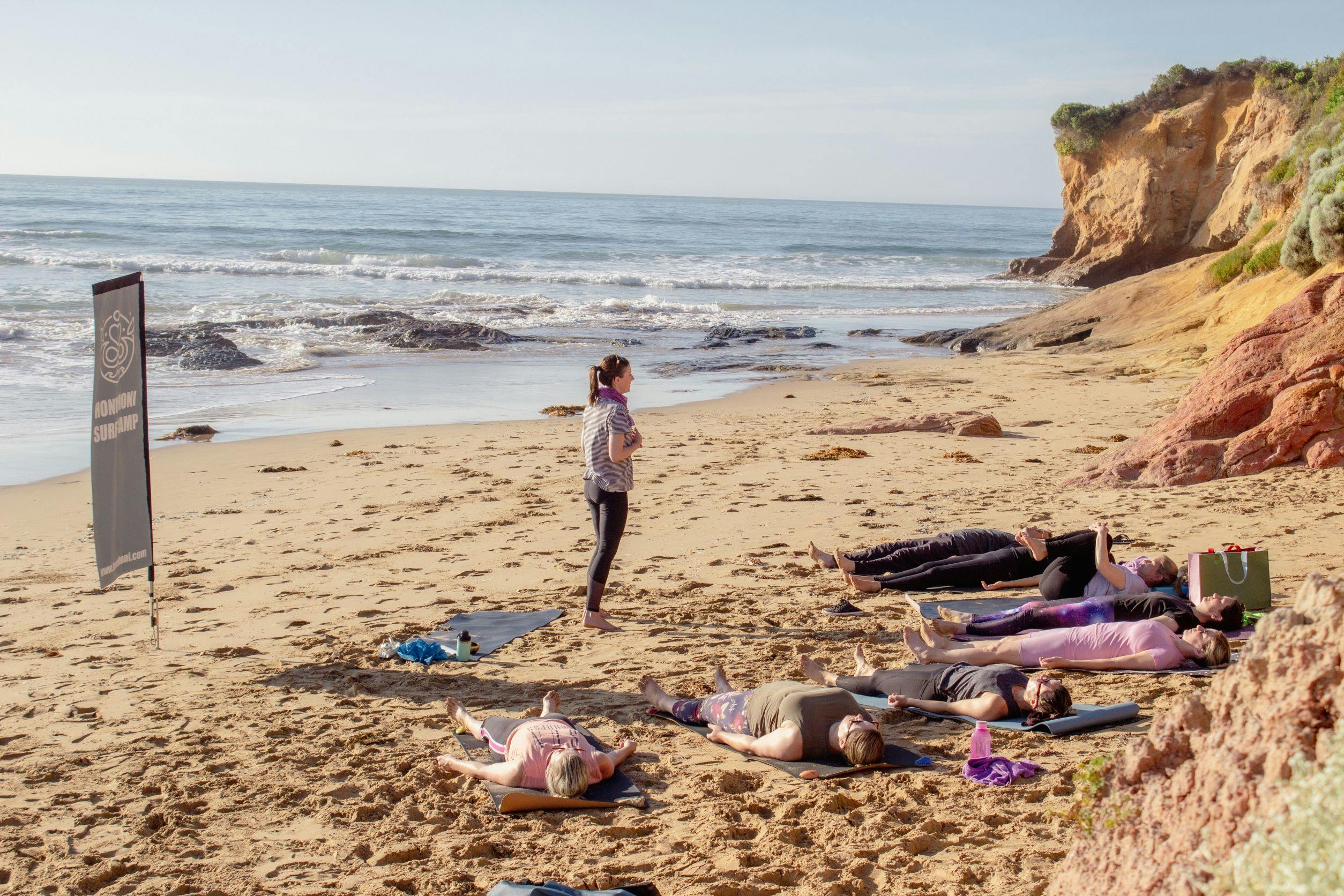 Students soaking in the end of a beach yoga session with the waves providing a beautiful sound scape