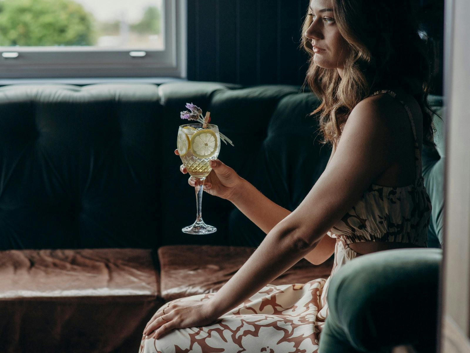 Woman sitting on a chair looking into the distance, holding a purple cocktail