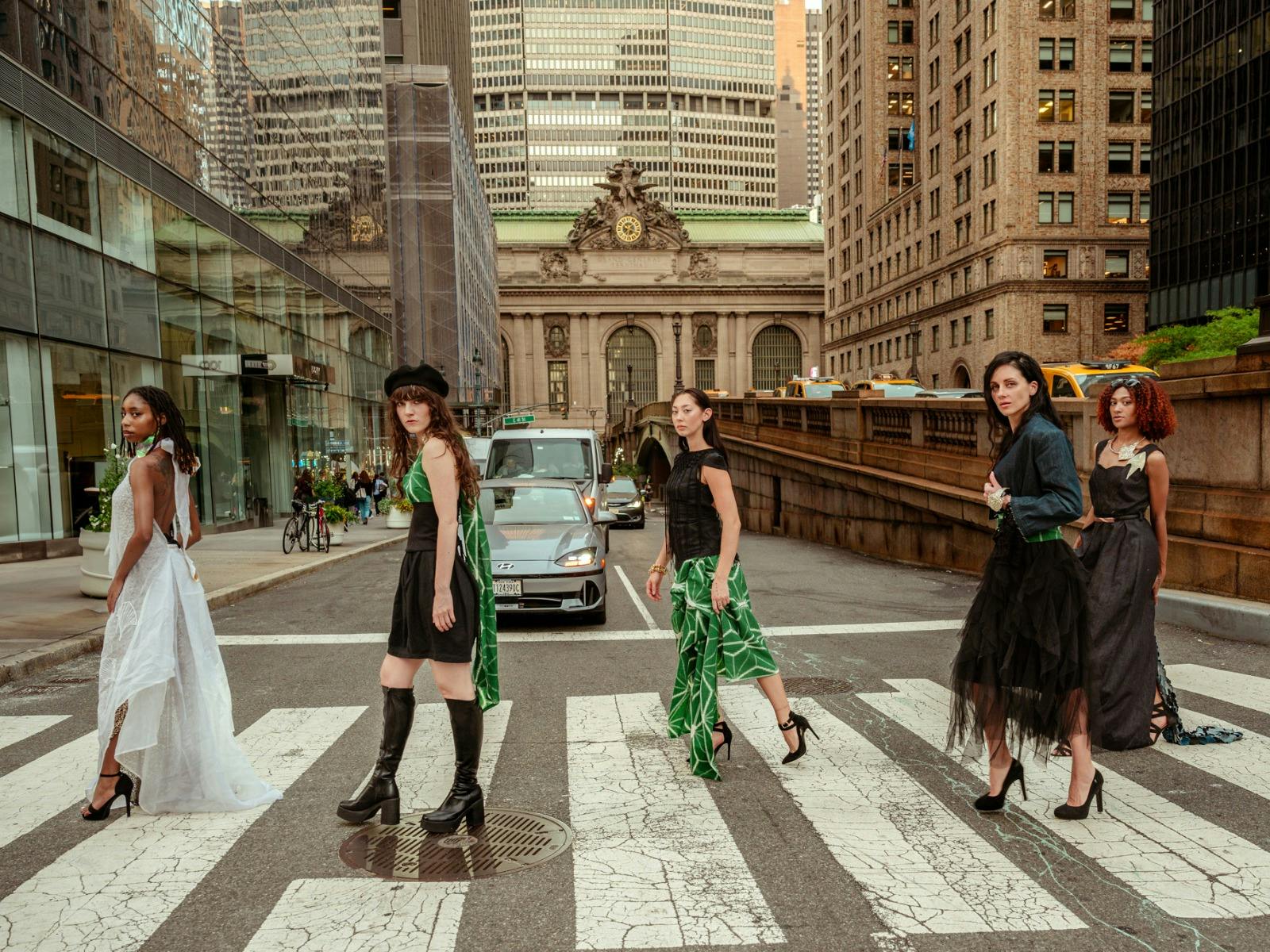 5 women on a crosswalk in New York. They wear dynamic green, black, and white flowing clothing,